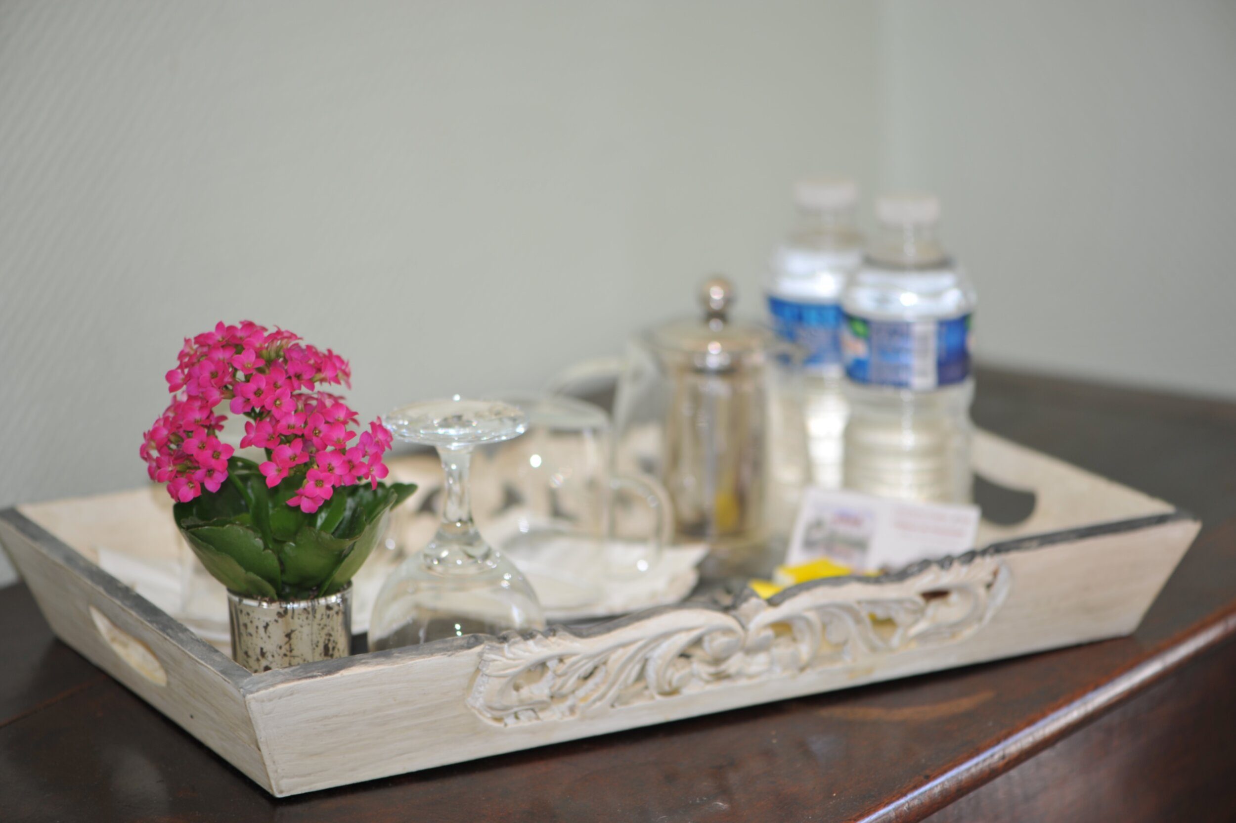Plateau en bois avec petit pot de fleurs, un verre, une tasses, deux petites bouteilles d'eau et une petite théière
