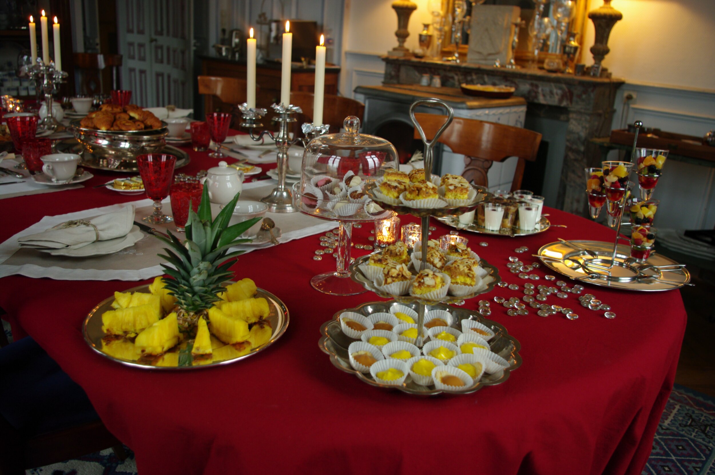 Table de brunch dressées avec une nappe rouge, des gâteaux maisons, des fruits fraîchement coupés et des bougies