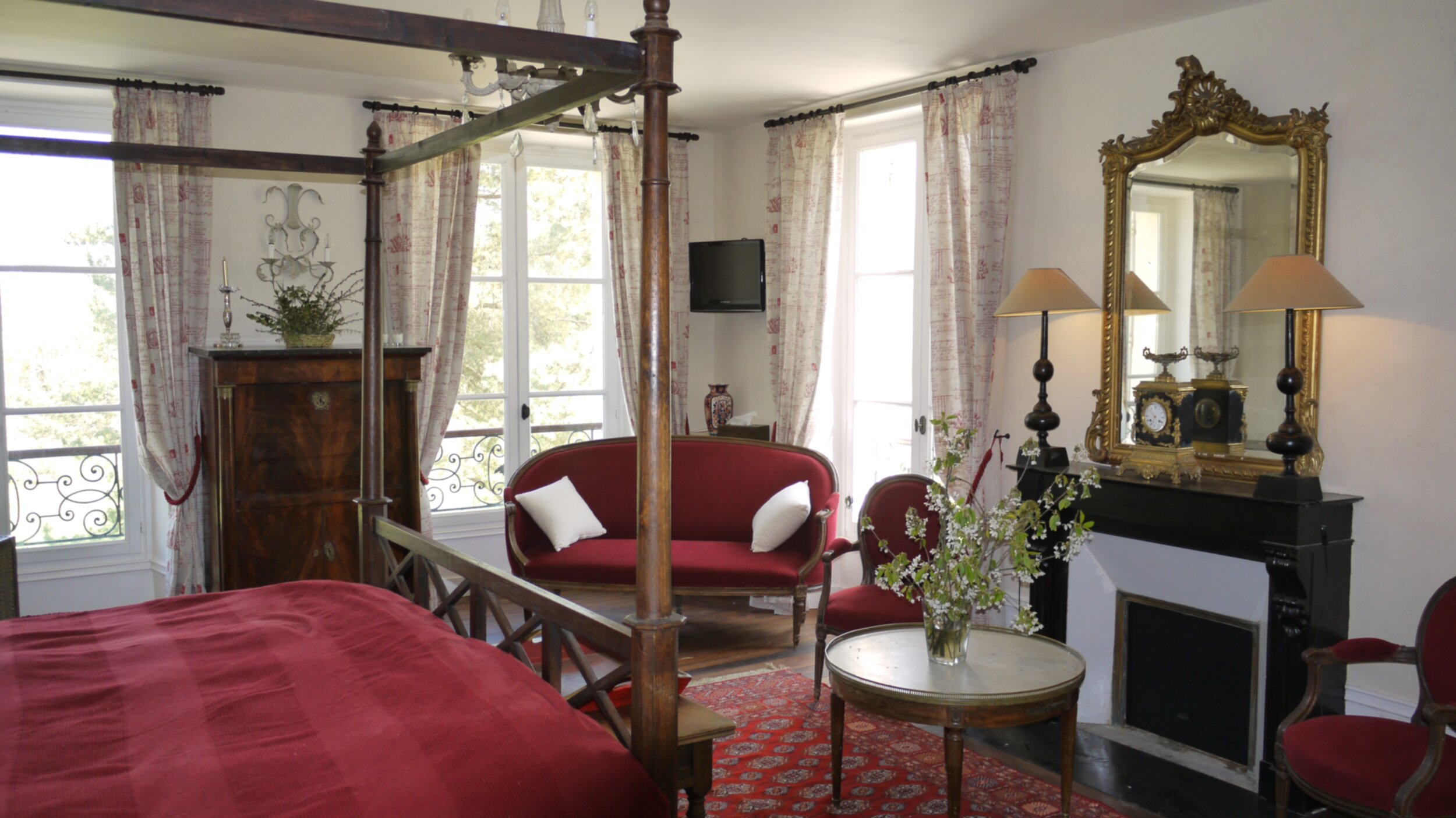 Chambre d'hôtes avec tapis, dessus de lit et canapé rouge, avec cheminée et lit à baldaquin